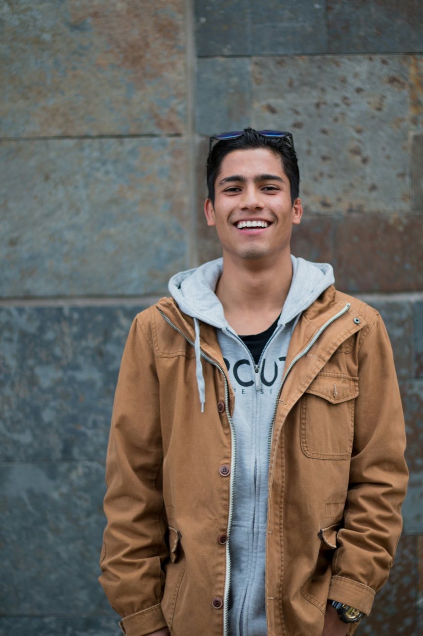 Young man in a coat smiling by a wall