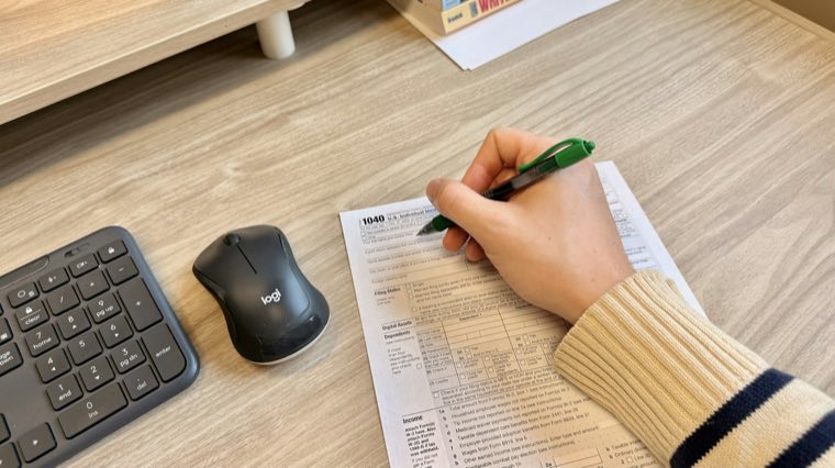 A hand filling in a form at a desk beside a keyboard